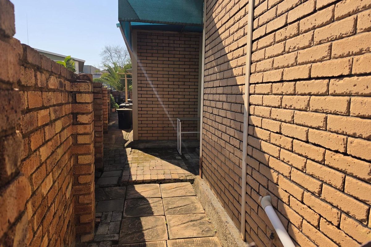 A narrow side passage featuring brick walls and paved flooring, providing access along the exterior of the property.