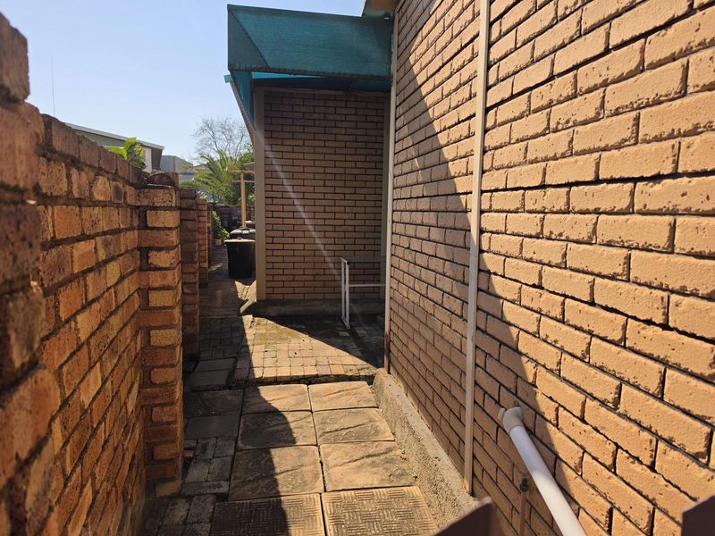 A narrow side passage featuring brick walls and paved flooring, providing access along the exterior of the property.