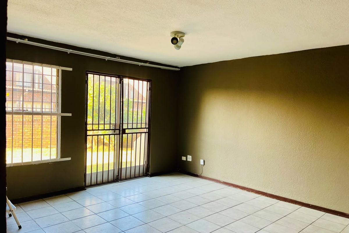 An empty living room featuring tiled flooring, security gates, and burglar bars on the windows, providing a blank canvas for interior design.