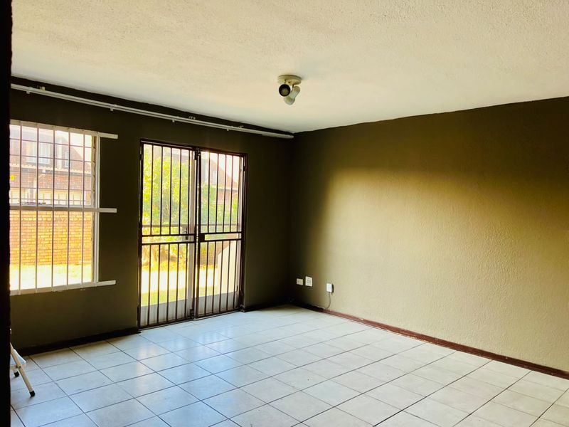 An empty living room featuring tiled flooring, security gates, and burglar bars on the windows, providing a blank canvas for interior design.