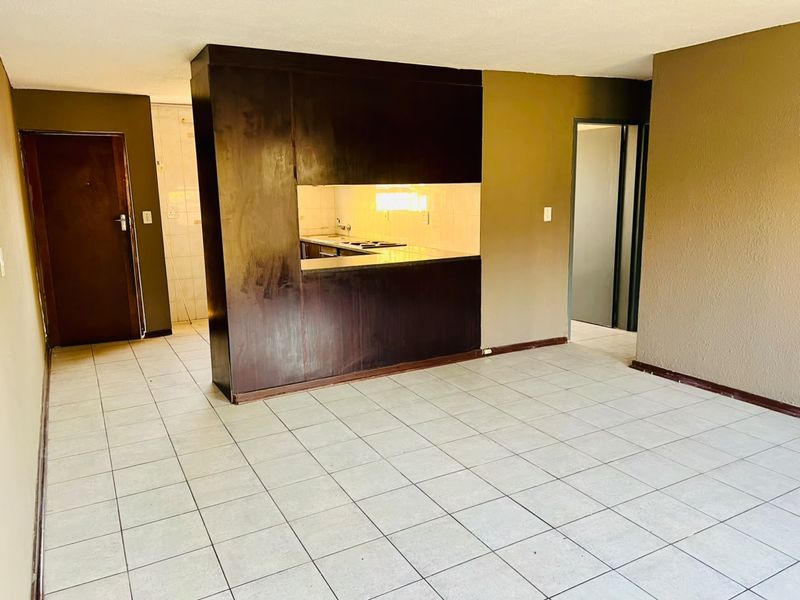 An open-plan living area featuring tiled flooring and a central kitchen unit with built-in cabinetry and a pass-through window.