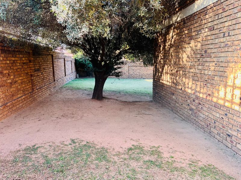 A private rear garden area featuring established brick boundary walls, a mature tree, and a lawn space.
