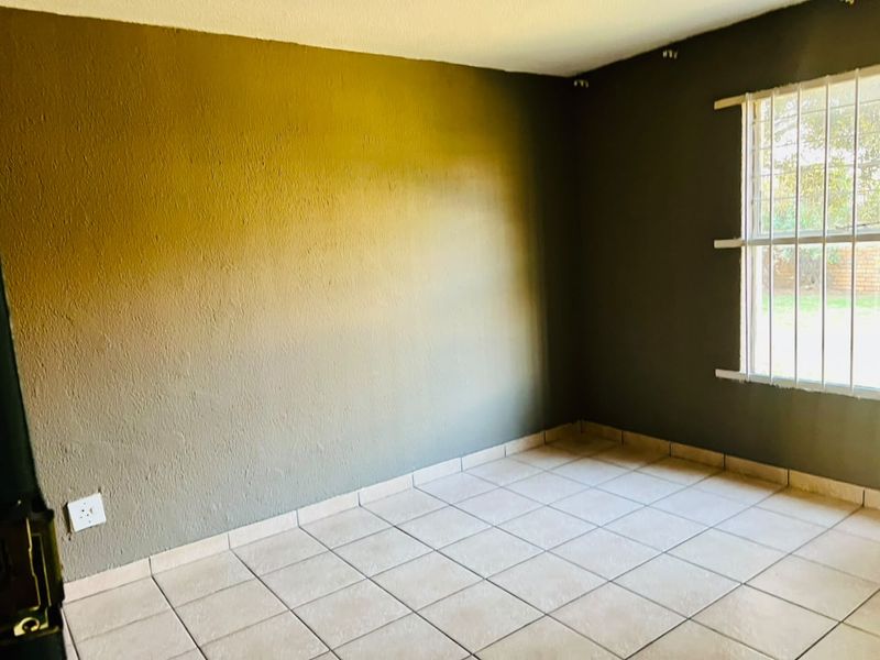 An empty bedroom featuring tiled flooring and a window fitted with security bars, awaiting personal touches to enhance the space.