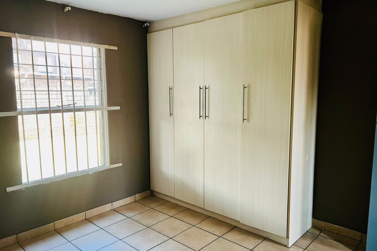 A vacant bedroom featuring built-in cupboards, tiled flooring, and a window fitted with security bars.