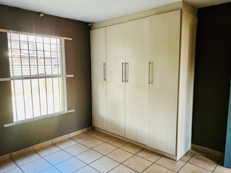 A vacant bedroom featuring built-in cupboards, tiled flooring, and a window fitted with security bars.