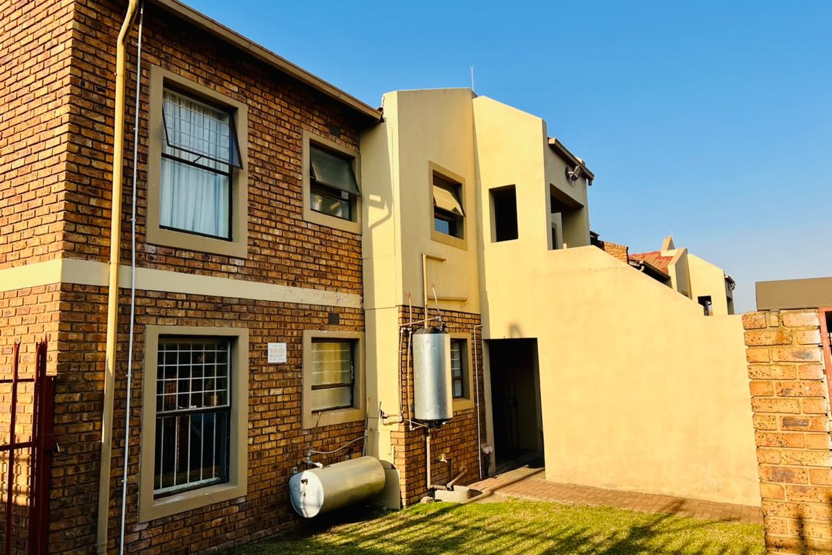 Rear view of the apartment building featuring exposed brickwork, plastered sections, an external geyser, and a paved garden area.