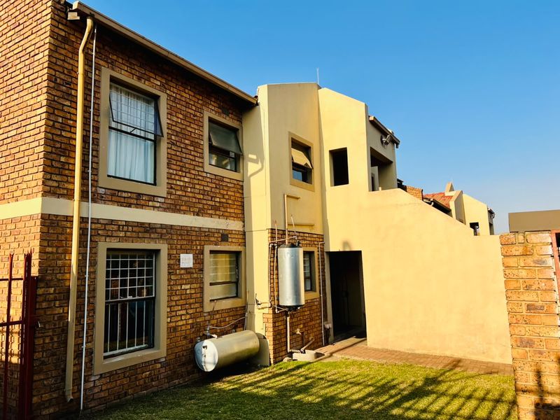 Rear view of the apartment building featuring exposed brickwork, plastered sections, an external geyser, and a paved garden area.