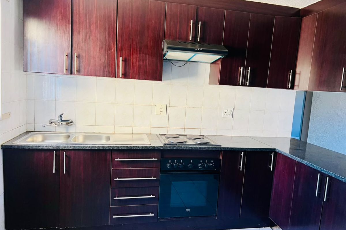 A functional kitchen featuring dark wood-finish cabinetry, granite-look countertops, a built-in oven with hob, and a stainless steel sink with tiled backsplash.