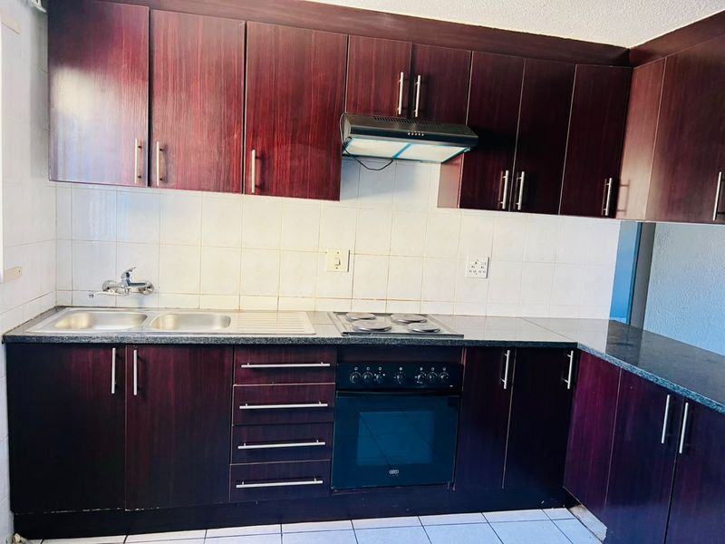 A functional kitchen featuring dark wood-finish cabinetry, granite-look countertops, a built-in oven with hob, and a stainless steel sink with tiled backsplash.