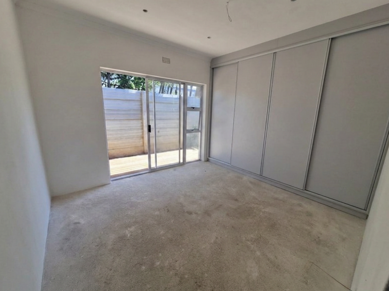 A bright, empty bedroom featuring built-in sliding door cupboards, recessed lighting, and direct access to an outdoor patio area through a sliding glass door.