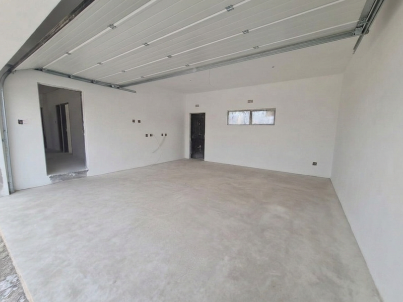 A spacious, unfinished double garage featuring a sectional door, concrete flooring, and direct access to the interior of the home.
