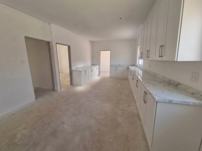 A spacious, newly installed kitchen featuring white cabinetry and marble-effect countertops, currently awaiting final flooring and lighting finishes.