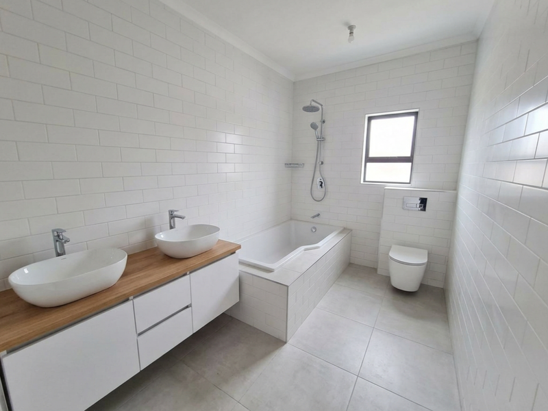 Modern bathroom featuring a double vanity with vessel sinks, a built-in bathtub with shower, and a wall-hung toilet, finished with clean subway tiling.