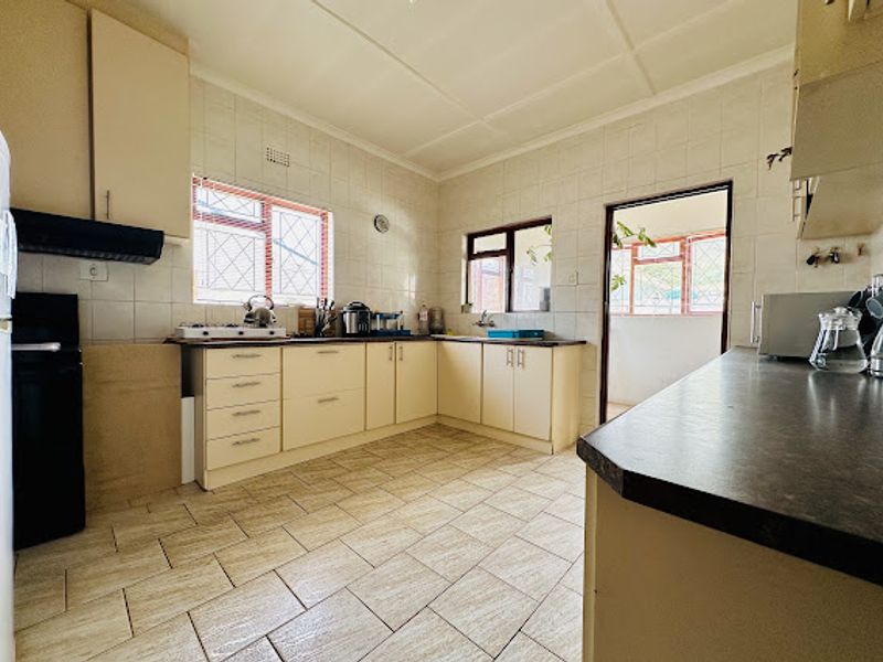 A functional kitchen featuring tiled flooring, ample built-in cabinetry, laminate countertops, and tiled wall finishes, offering a practical layout with direct access to an adjacent area.
