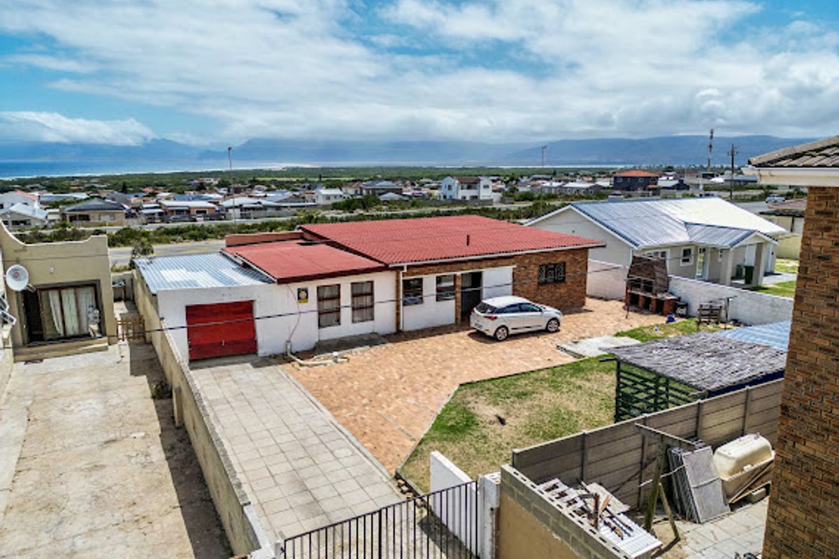 Aerial view of the rear property featuring a red metal roof, paved driveway, brick facade, and an outdoor braai area with surrounding boundary walls.