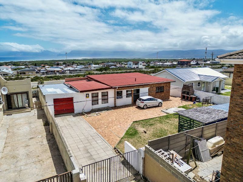 Aerial view of the rear property featuring a red metal roof, paved driveway, brick facade, and an outdoor braai area with surrounding boundary walls.