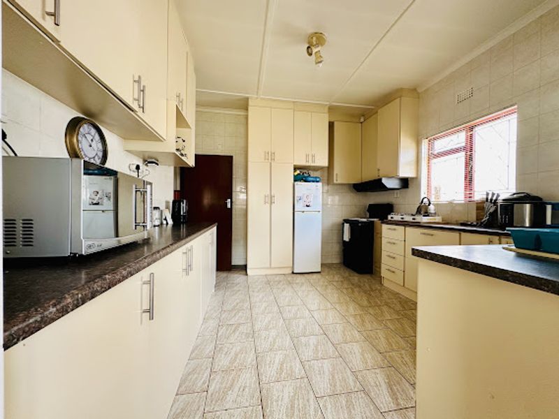 A functional kitchen featuring ample built-in cabinetry, laminate countertops, tiled flooring, and a tiled backsplash, offering a practical layout for daily meal preparation.