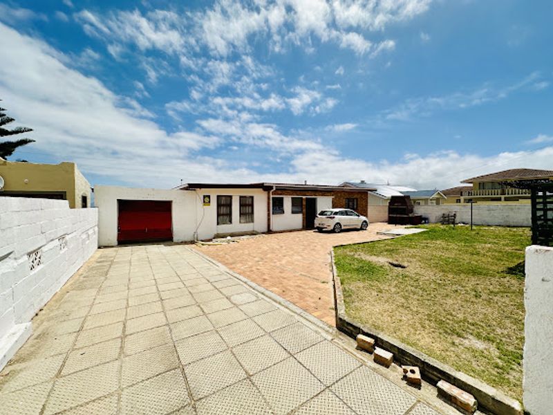 Rear exterior view of the property featuring a paved driveway, brick patio area, attached garage, and a private lawn enclosed by boundary walls.