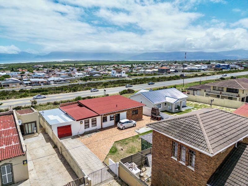 Aerial view of the property showing the main house, paved driveway, and surrounding residential neighborhood with distant mountain and coastal views.