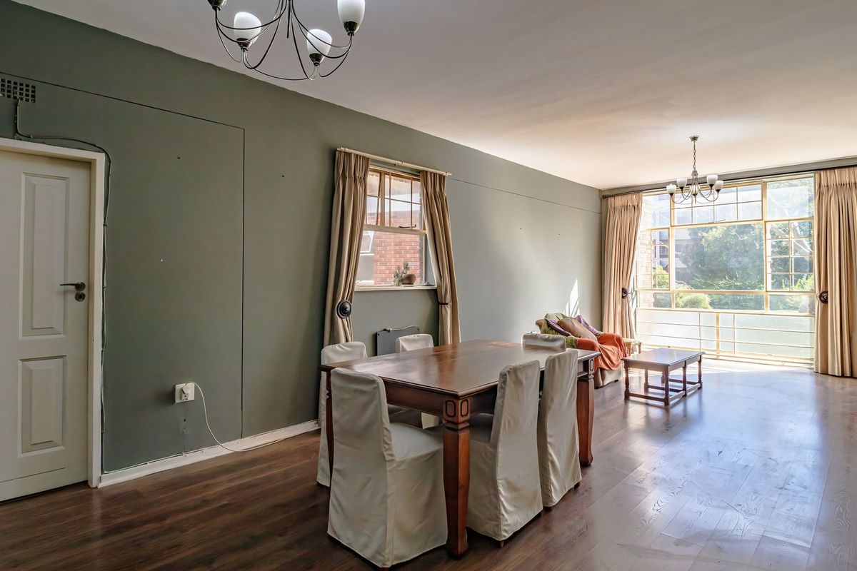 Spacious living and dining area featuring dark laminate flooring, large windows providing natural light, and classic ceiling light fixtures.