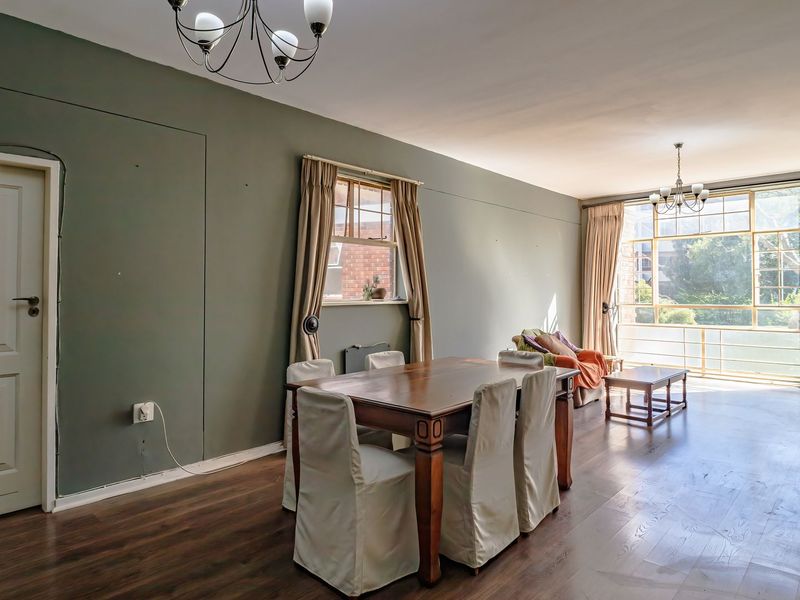 Spacious living and dining area featuring dark laminate flooring, large windows providing natural light, and classic ceiling light fixtures.