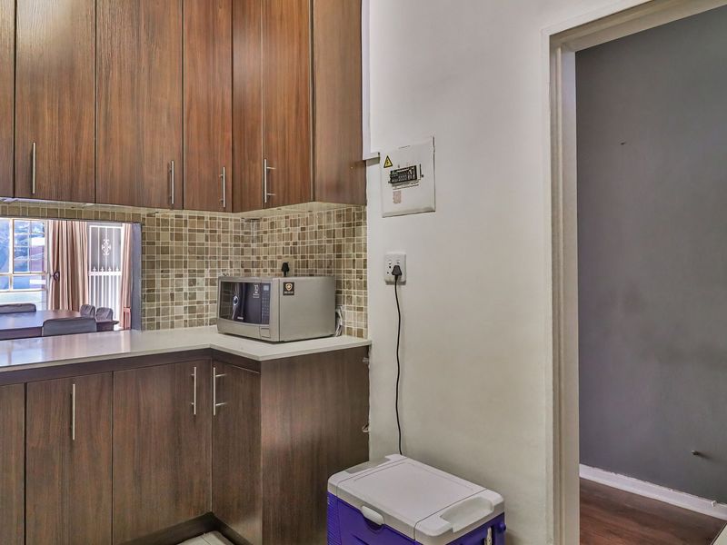 A functional kitchen area featuring wood-finish cabinetry, a mosaic tile backsplash, and a convenient serving window looking into the adjacent living space.