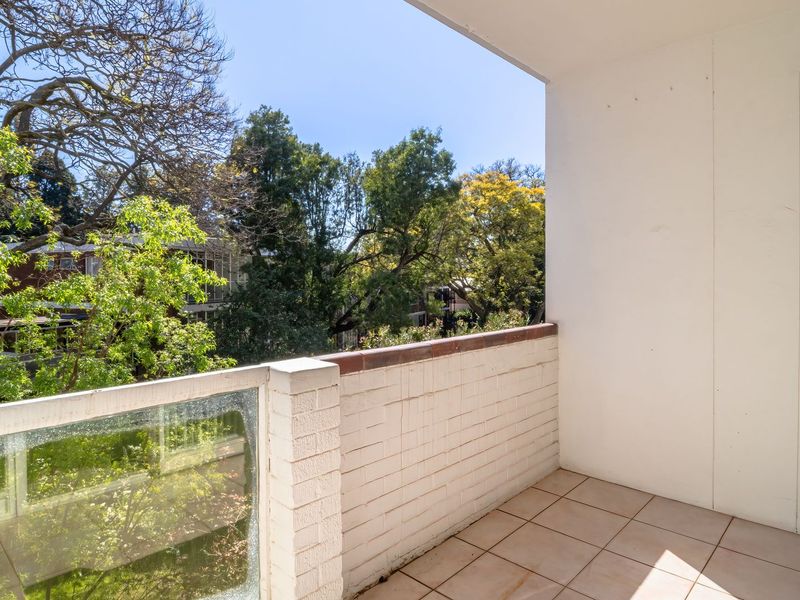 A private balcony featuring tiled flooring and a brick balustrade with glass paneling, offering a pleasant outlook over the surrounding trees.