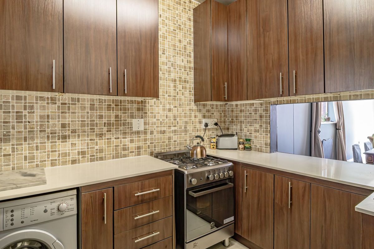 A functional kitchen featuring wood-finish cabinetry, stone countertops, a mosaic tile backsplash, and a built-in gas stove with oven.