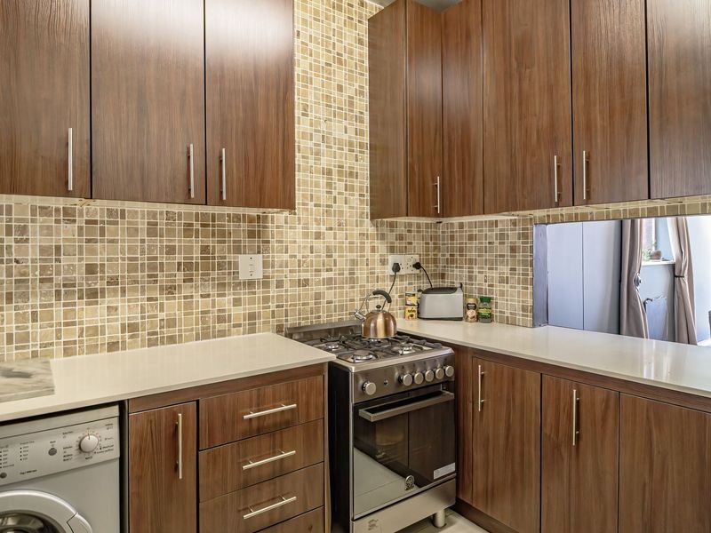 A functional kitchen featuring wood-finish cabinetry, stone countertops, a mosaic tile backsplash, and a built-in gas stove with oven.