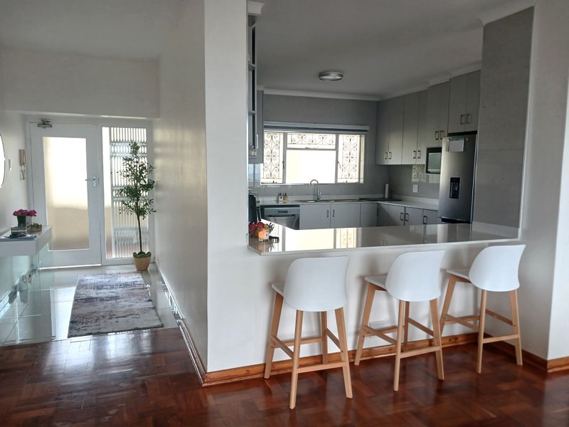 Open plan kitchen featuring a breakfast bar, modern cabinetry, and stone countertops, seamlessly connected to the entrance area with parquet and tiled flooring.