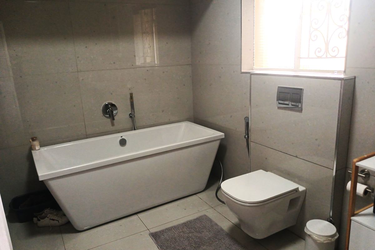 Modern bathroom featuring a sleek freestanding bathtub, wall-mounted toilet with concealed cistern, and neutral floor-to-ceiling tiling.