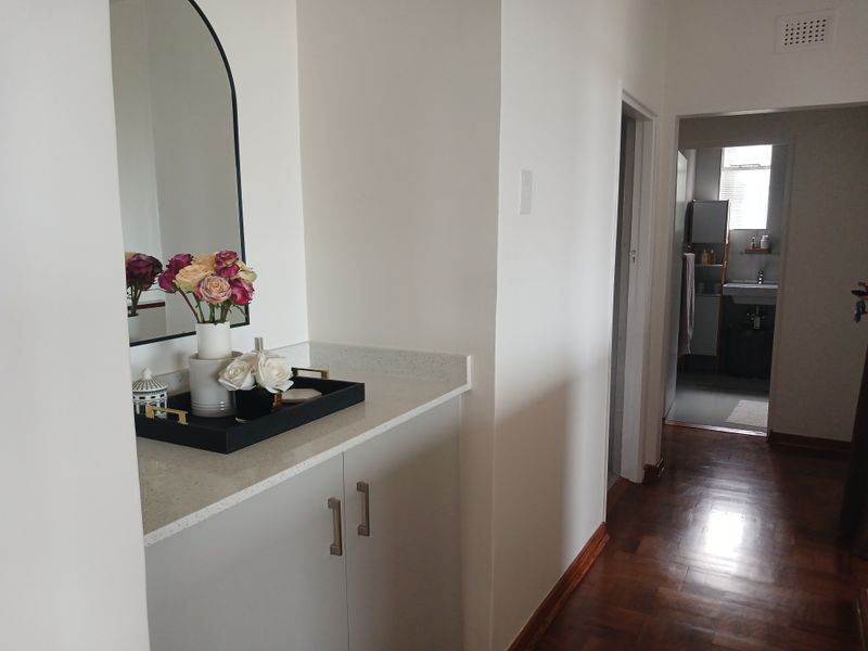 A well-maintained hallway featuring built-in cabinetry with a stone countertop, parquet flooring, and a view leading into a bathroom.