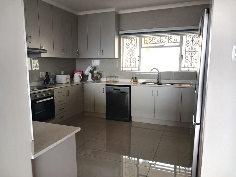 Modern kitchen featuring sleek grey cabinetry, stone countertops, integrated appliances, and large floor tiles, offering a clean and functional workspace.