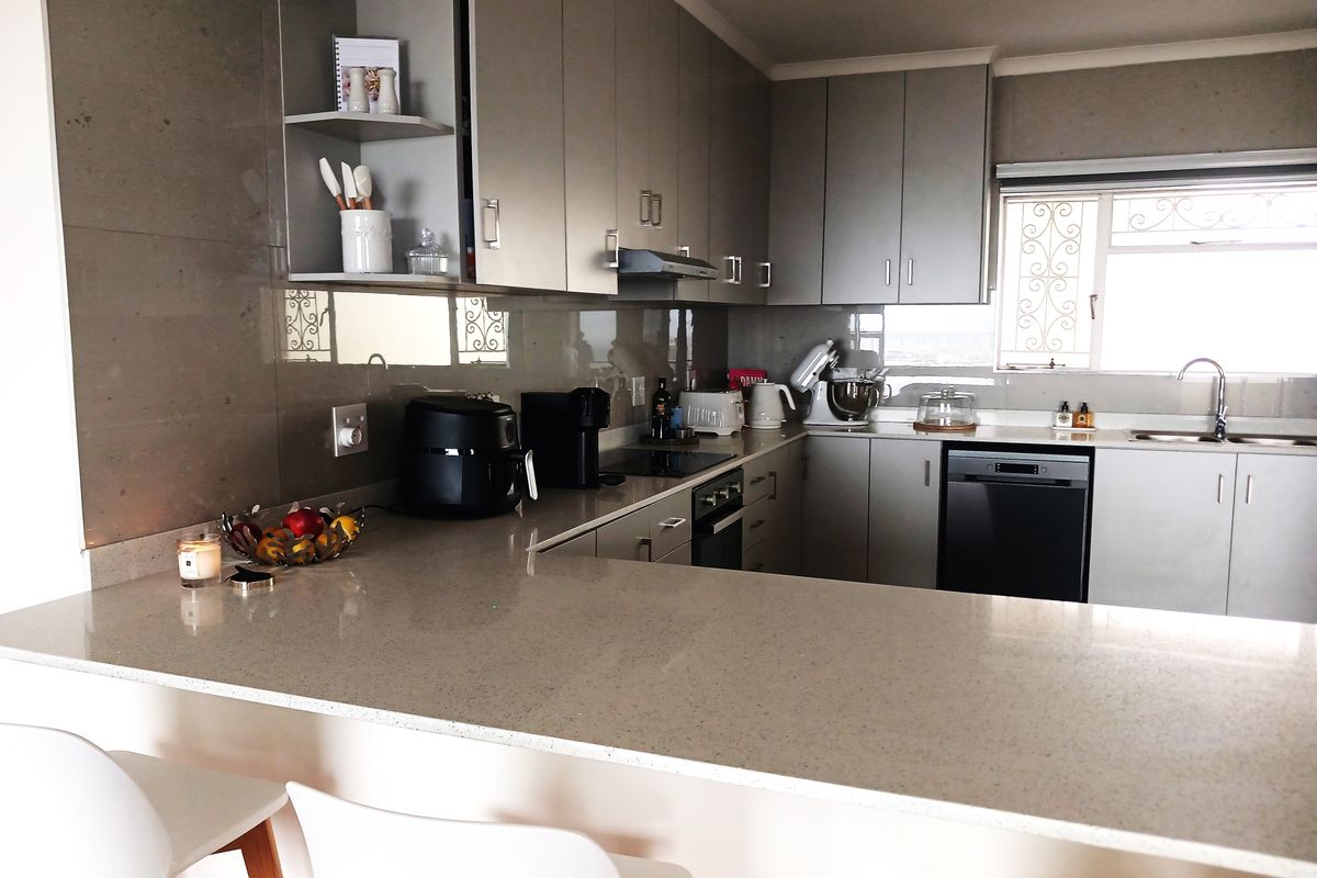 Modern kitchen featuring sleek grey cabinetry, quartz countertops, a breakfast bar, and integrated appliances, offering a functional and contemporary cooking space.