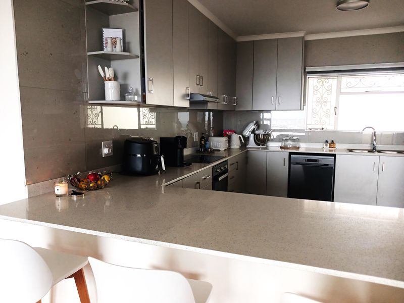 Modern kitchen featuring sleek grey cabinetry, quartz countertops, a breakfast bar, and integrated appliances, offering a functional and contemporary cooking space.