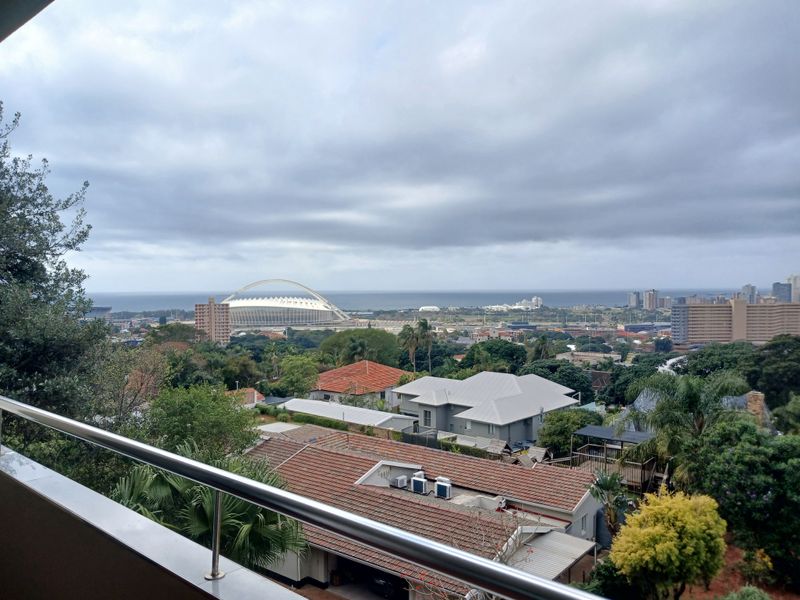 Elevated urban and coastal view featuring a balcony with a stainless steel railing overlooking the surrounding neighborhood and stadium.