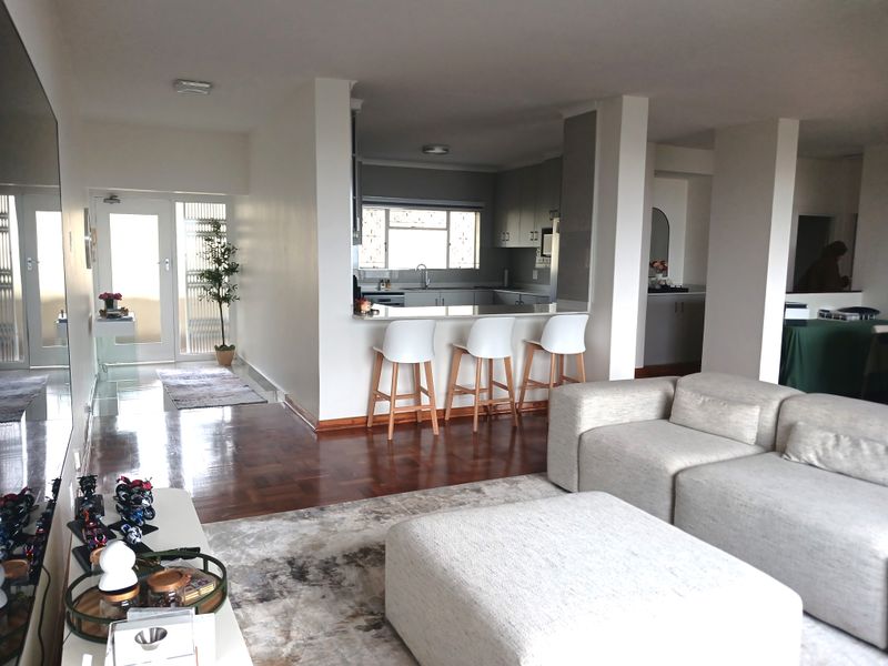 Open-plan living area featuring parquet flooring, a breakfast bar, and a functional kitchen with built-in cabinetry, seamlessly connected to the entrance hall.