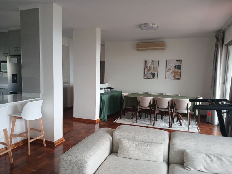 Open-plan living and dining area featuring warm parquet flooring, a modern kitchen island, and a wall-mounted air conditioning unit.