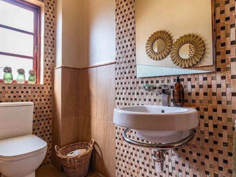 A compact bathroom featuring mosaic wall tiling, a wall-mounted basin with chrome fixtures, and a standard ceramic toilet.