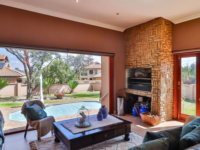 Covered patio area featuring a built-in stone-clad braai, tiled flooring, and large sliding doors opening directly onto the pool and garden area.