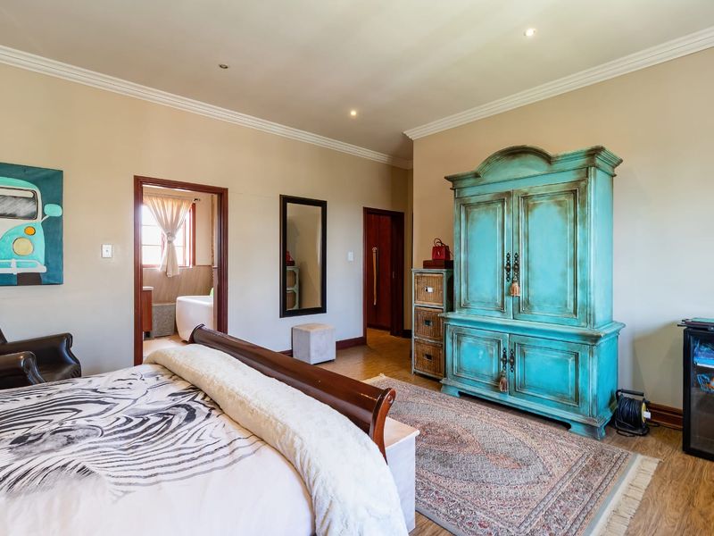 Spacious bedroom featuring laminate flooring, crown molding, and recessed lighting, with an adjoining en-suite bathroom visible through the doorway.