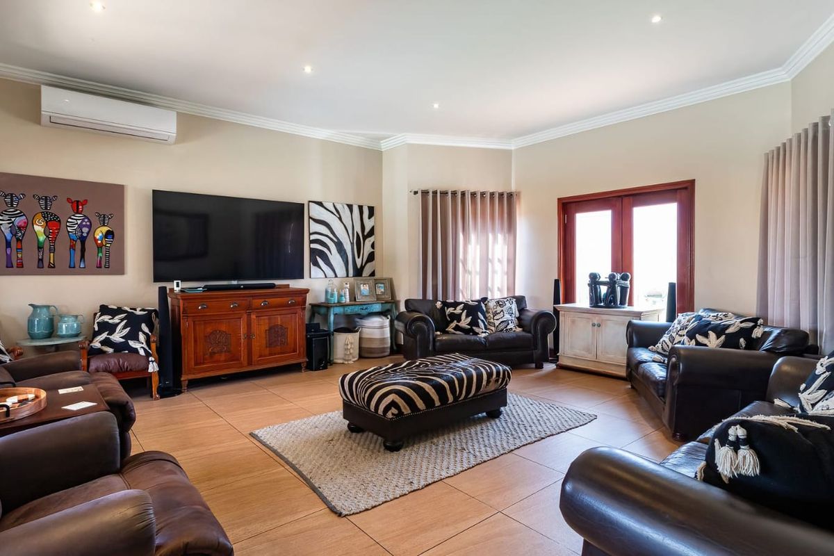 A spacious living room featuring tiled flooring, recessed downlighting, crown molding, and a wall-mounted split-system air conditioner with access to the outdoors via double doors.