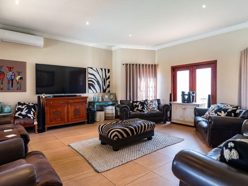 A spacious living room featuring tiled flooring, recessed downlighting, crown molding, and a wall-mounted split-system air conditioner with access to the outdoors via double doors.