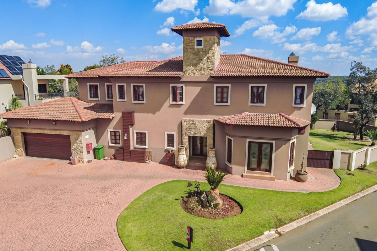 Aerial view of a large multi-story residential property featuring a tiled roof, brick driveway, and well-maintained landscaped garden.