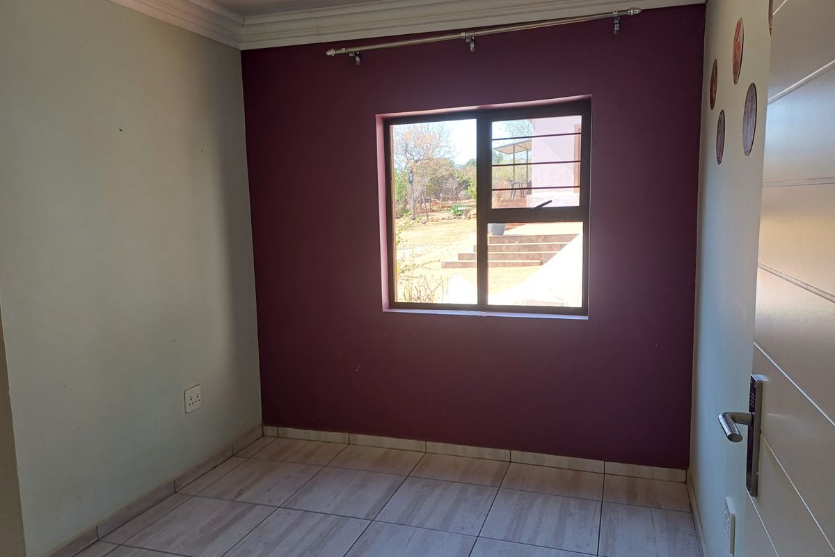 An empty bedroom featuring tiled flooring, a window with security bars, and decorative cornice detailing.