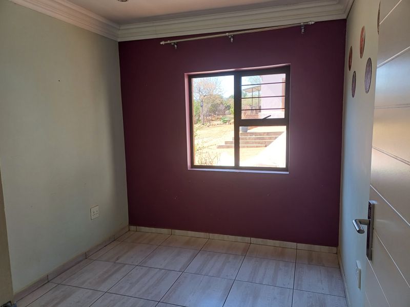 An empty bedroom featuring tiled flooring, a window with security bars, and decorative cornice detailing.