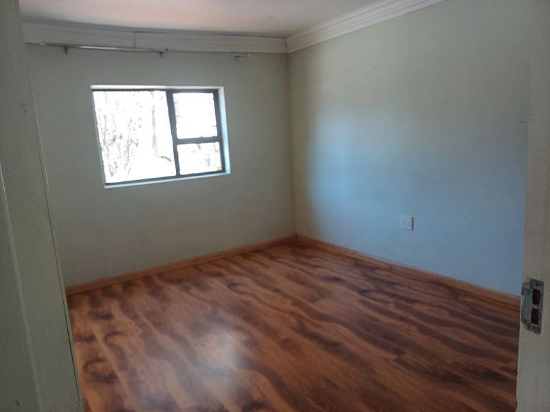 An empty bedroom featuring laminate flooring, neutral wall paint, and a window fitted with security burglar bars.