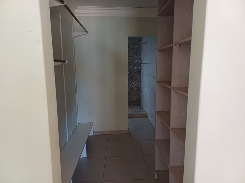 A walk-in dressing area featuring built-in shelving and hanging rails, leading directly into an en-suite shower room with tiled finishes.