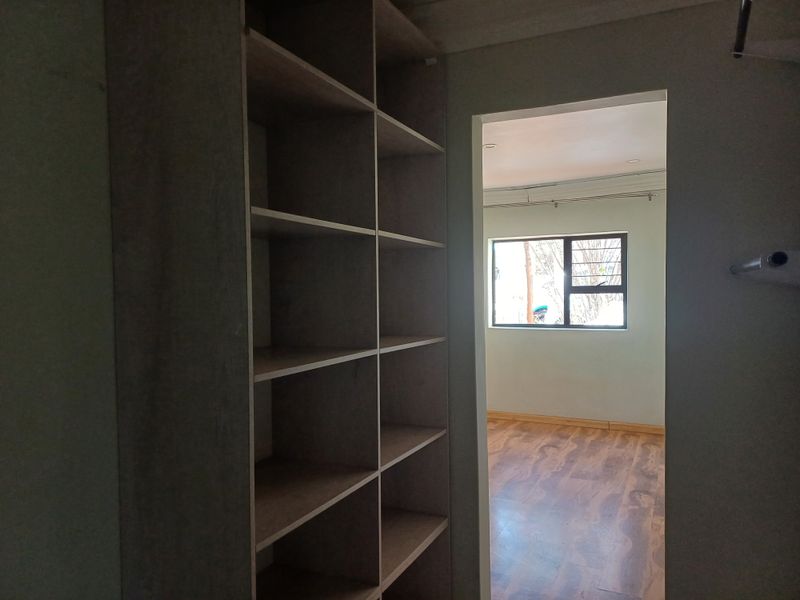 A view from a walk-in closet area looking into a bedroom featuring laminate flooring and an aluminium-framed window.