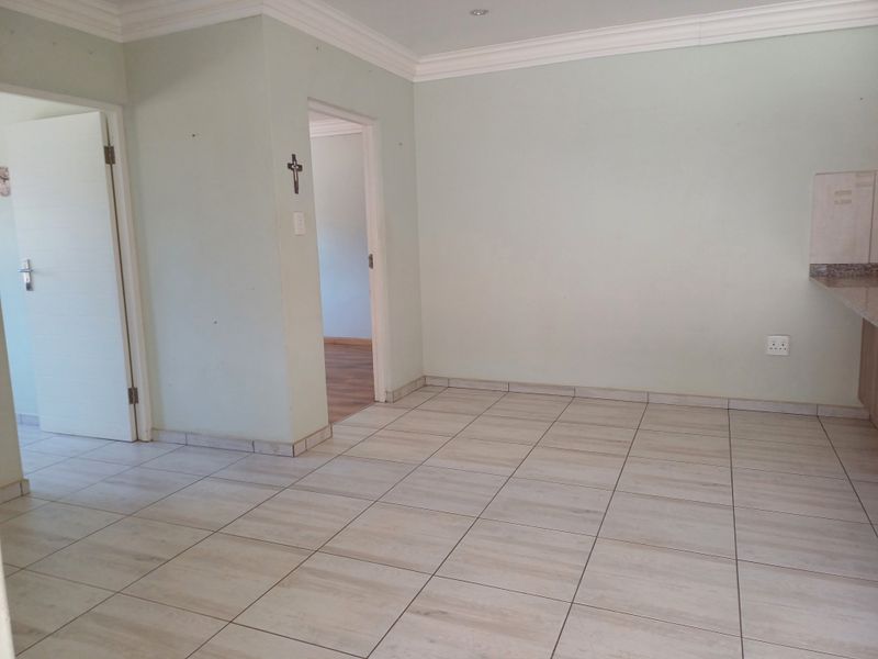 An empty open-plan living area featuring neutral tiled flooring, decorative cornicing, and recessed lighting, providing a blank canvas for interior design.